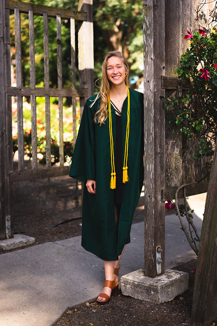 Cal Poly grad in gown by wooden arch