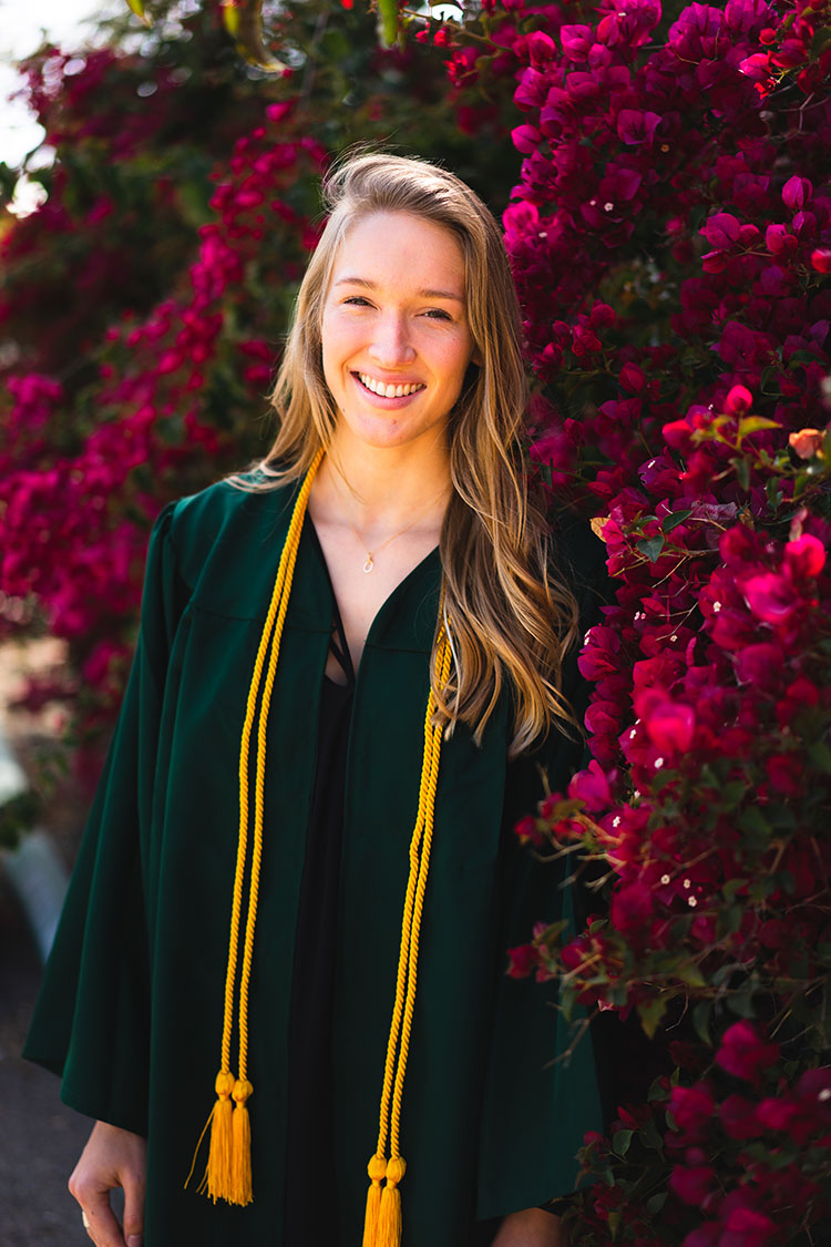 Cal Poly grad in gown in front of bougainvillea bush