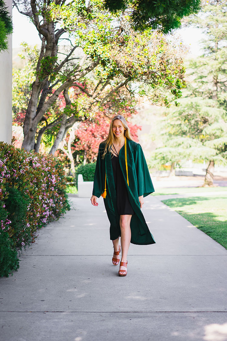 Cal Poly grad in gown struts under trees toward camera